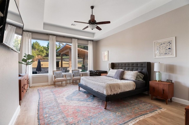 bedroom with ceiling fan, a raised ceiling, and light wood-type flooring