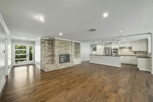 unfurnished living room featuring ornamental molding, dark wood-style flooring, visible vents, and a stone fireplace