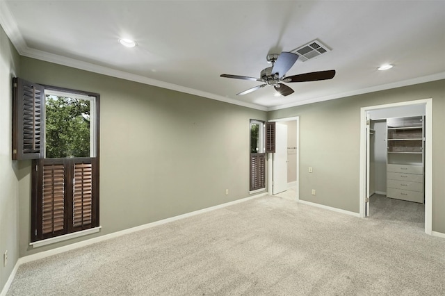 unfurnished bedroom featuring ceiling fan, light colored carpet, a walk in closet, a closet, and ornamental molding