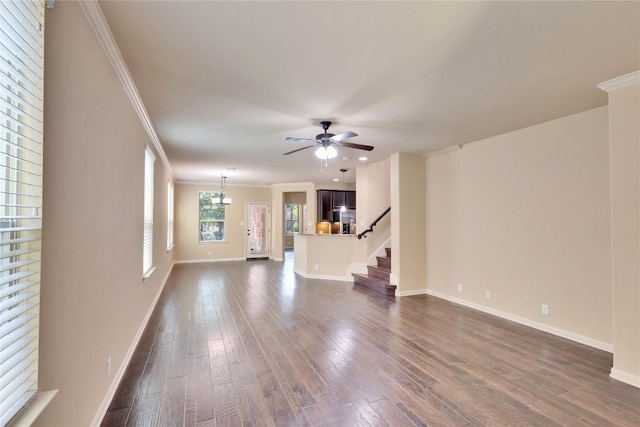 unfurnished living room with ceiling fan with notable chandelier, dark wood-type flooring, and ornamental molding