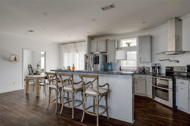 15701 Forest Glenn Cv, Del Valle, TX 78617 - kitchen with appliances with stainless steel finishes, wall chimney exhaust hood, gray cabinetry, crown molding, and dark wood-type flooring