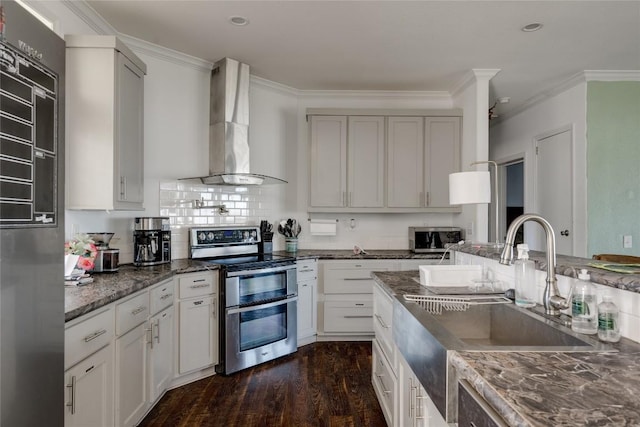 15701 Forest Glenn Cv, Del Valle, TX 78617 - kitchen featuring stainless steel appliances, wall chimney exhaust hood, dark wood-style flooring, ornamental molding, and dark stone countertops