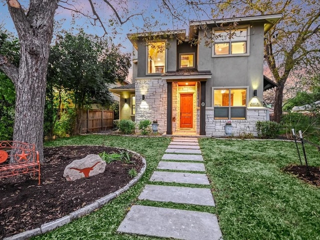 view of front of property with stone siding, a yard, fence, and stucco siding