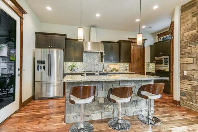 kitchen with appliances with stainless steel finishes, an island with sink, light wood-style flooring, and decorative backsplash