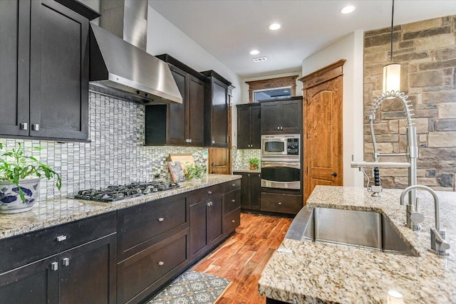 kitchen with decorative light fixtures, stainless steel appliances, backsplash, light wood-type flooring, and wall chimney exhaust hood