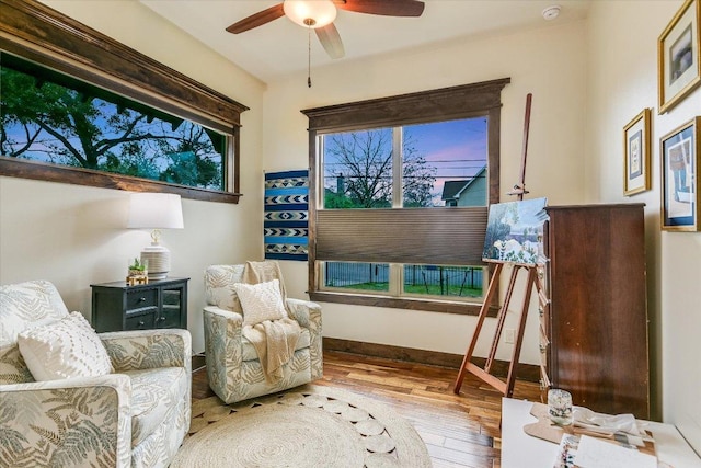 living area with wood-type flooring, ceiling fan, and baseboards