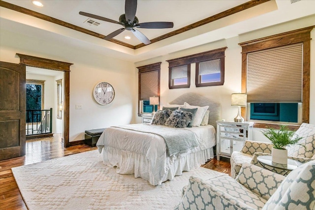 bedroom with wood finished floors, visible vents, baseboards, ornamental molding, and a raised ceiling