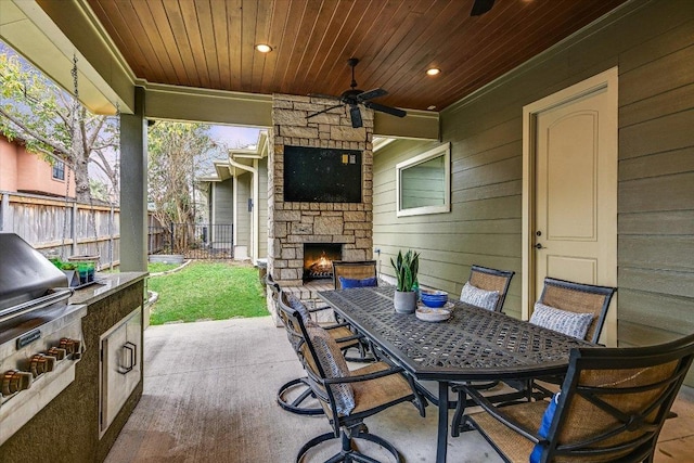 view of patio / terrace featuring an outdoor stone fireplace, fence, a ceiling fan, exterior kitchen, and outdoor dining space