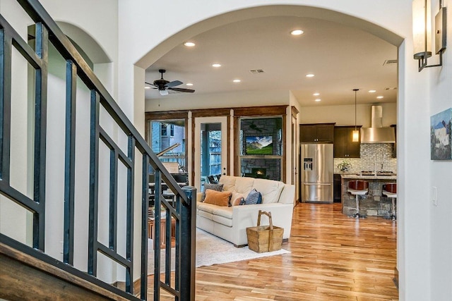 living area featuring arched walkways, recessed lighting, a ceiling fan, light wood-type flooring, and stairs