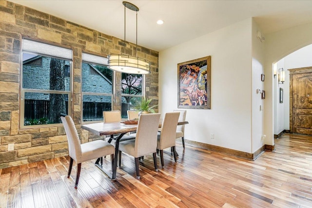 dining room with light wood-style floors, arched walkways, and baseboards