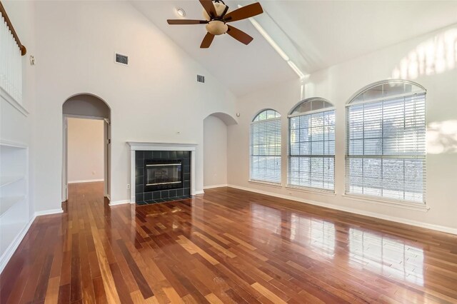 unfurnished living room with high vaulted ceiling, ceiling fan, a wealth of natural light, and a tiled fireplace