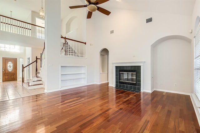 unfurnished living room featuring ceiling fan, built in shelves, a towering ceiling, and hardwood / wood-style floors