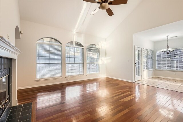 unfurnished living room with ceiling fan with notable chandelier, a fireplace, hardwood / wood-style floors, and high vaulted ceiling