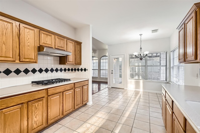 kitchen with pendant lighting, a wealth of natural light, tasteful backsplash, a chandelier, and stainless steel gas stovetop