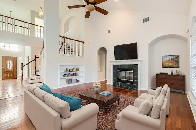 living room featuring a tile fireplace, hardwood / wood-style floors, ceiling fan, and built in shelves