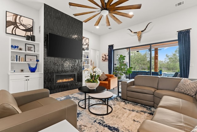 living area with built in shelves, visible vents, a fireplace, and wood finished floors