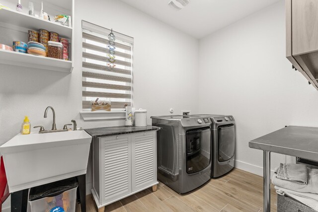 clothes washing area featuring washing machine and dryer, a sink, visible vents, baseboards, and light wood-type flooring