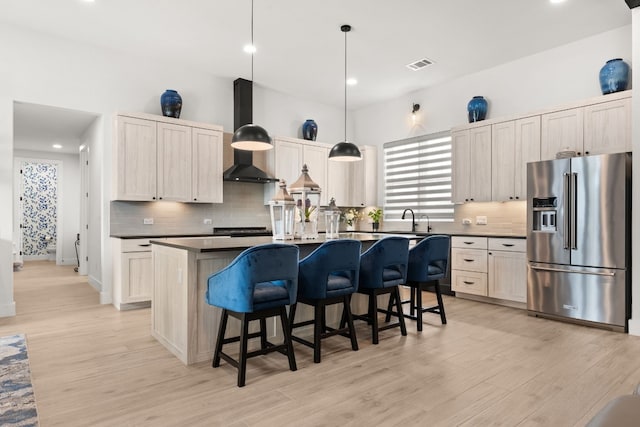 kitchen with range hood, high end fridge, dark countertops, a sink, and a kitchen breakfast bar