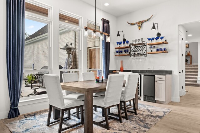 dining area with a dry bar, recessed lighting, light wood-style flooring, baseboards, and stairs