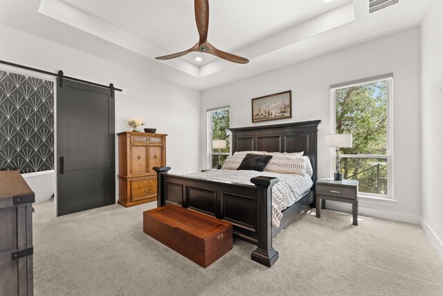 bedroom with a barn door, visible vents, a raised ceiling, and light colored carpet