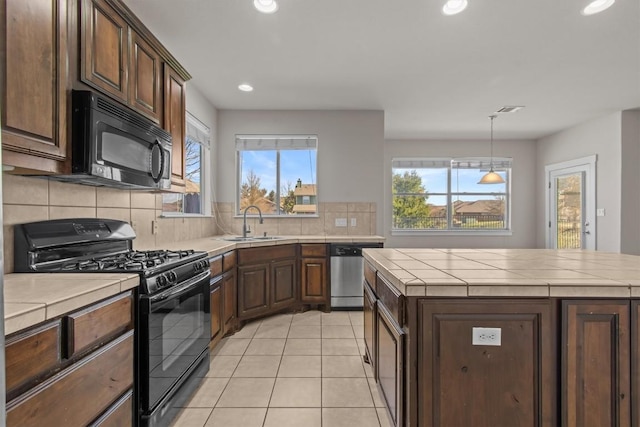 kitchen with tile counters, tasteful backsplash, decorative light fixtures, a kitchen island, and black appliances