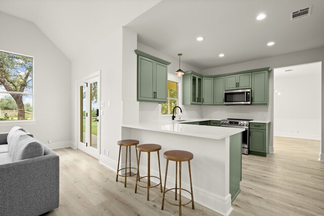 kitchen featuring lofted ceiling, hanging light fixtures, green cabinetry, appliances with stainless steel finishes, and kitchen peninsula