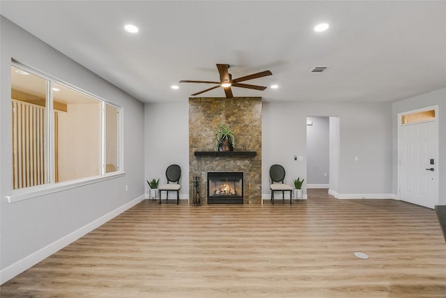 living room with ceiling fan, a large fireplace, and light wood-type flooring