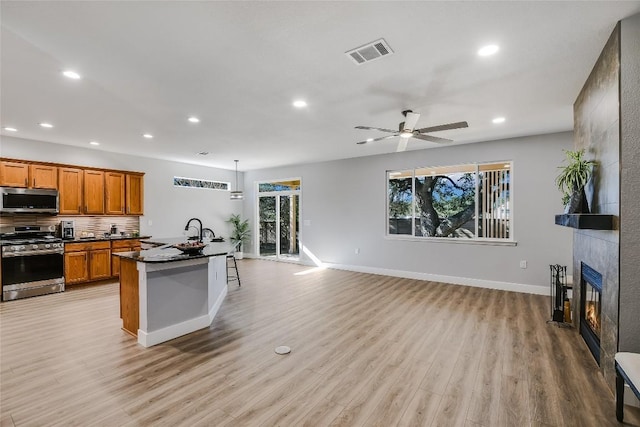 kitchen featuring appliances with stainless steel finishes, ceiling fan, light hardwood / wood-style floors, hanging light fixtures, and a tiled fireplace