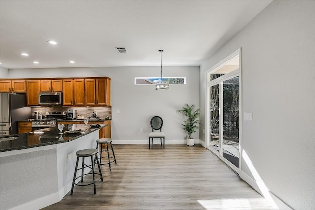 kitchen featuring stainless steel appliances, dark stone counters, pendant lighting, a breakfast bar area, and decorative backsplash