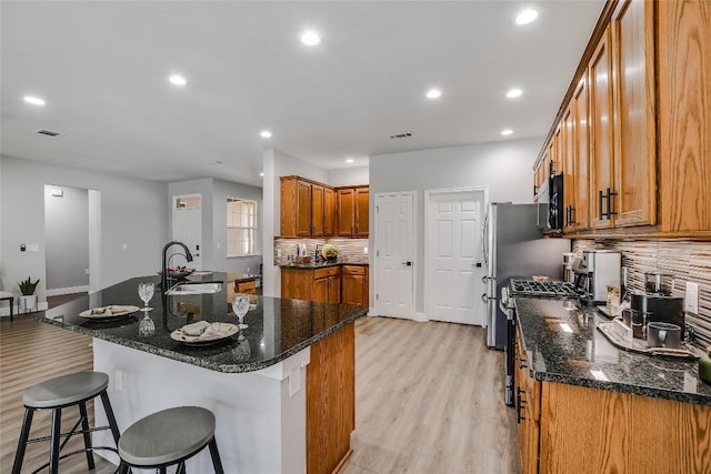 kitchen featuring sink, backsplash, dark stone counters, a kitchen bar, and a center island with sink