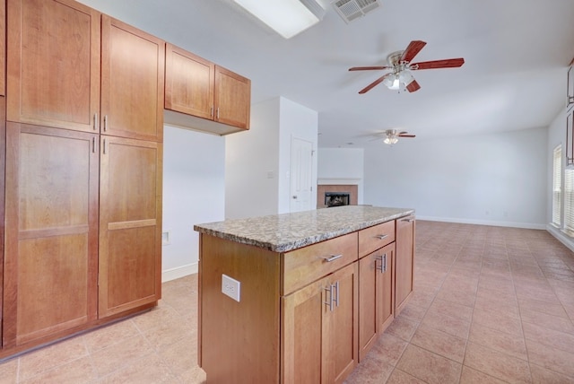 kitchen with ceiling fan, a kitchen island, light stone counters, and light tile patterned floors