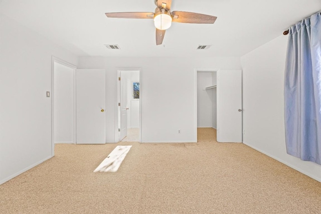 unfurnished bedroom featuring light carpet, a closet, a spacious closet, and ceiling fan