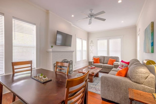 living room with a brick fireplace, crown molding, ceiling fan, and light wood-type flooring