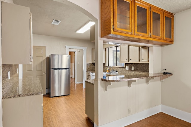 kitchen featuring backsplash, stainless steel fridge, light stone countertops, light hardwood / wood-style floors, and kitchen peninsula