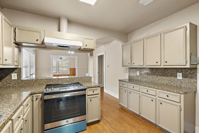 kitchen with stainless steel range with electric stovetop, ceiling fan, decorative backsplash, and cream cabinets