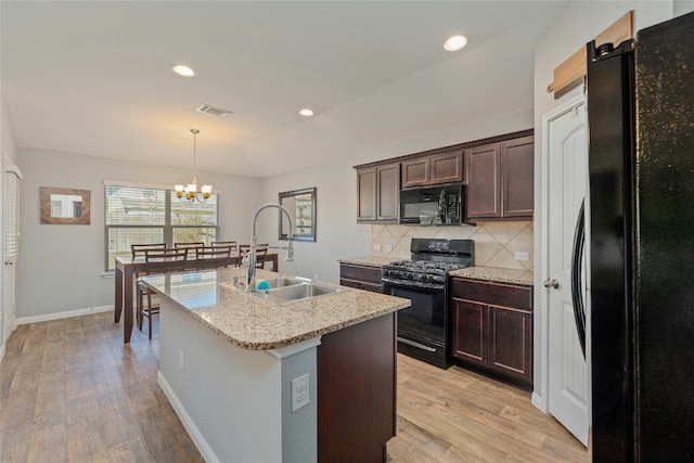 kitchen featuring tasteful backsplash, vaulted ceiling, a kitchen island with sink, sink, and black appliances