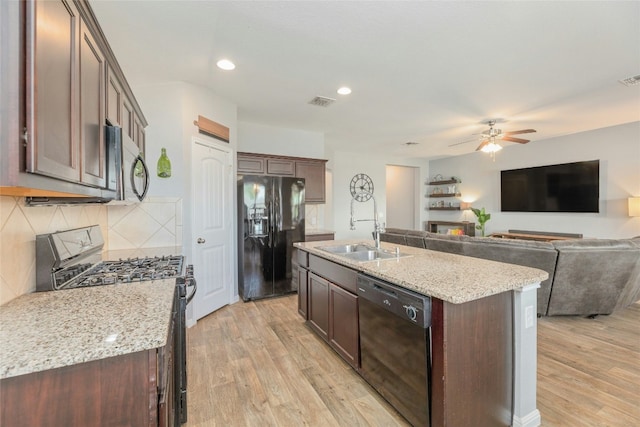 kitchen featuring light stone countertops, a center island with sink, black appliances, and light hardwood / wood-style flooring