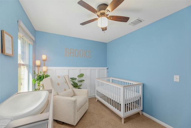 bedroom with a crib, light carpet, and ceiling fan