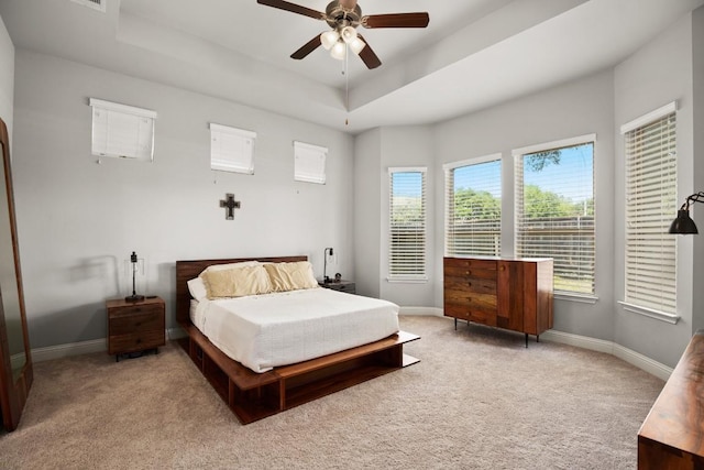 carpeted bedroom with a raised ceiling and ceiling fan