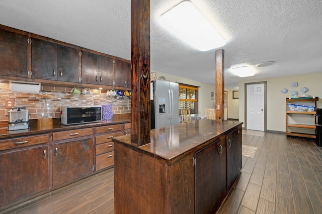 kitchen featuring tasteful backsplash, ornate columns, dark brown cabinetry, a kitchen island, and white fridge with ice dispenser