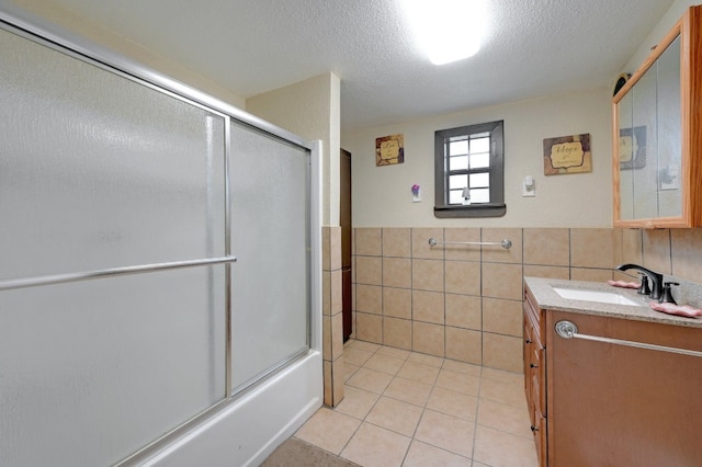 bathroom with tile patterned floors, a textured ceiling, vanity, tile walls, and enclosed tub / shower combo