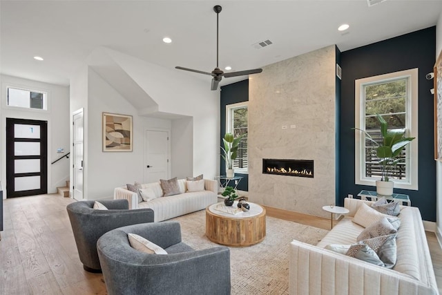 living room with a high end fireplace, ceiling fan, light hardwood / wood-style floors, and a wealth of natural light