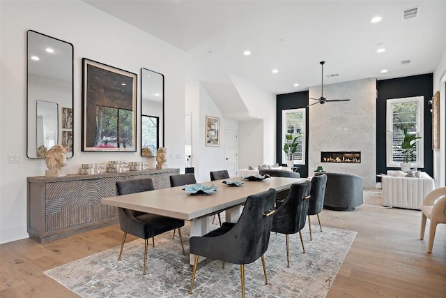 dining space featuring a high end fireplace, light wood-type flooring, and ceiling fan