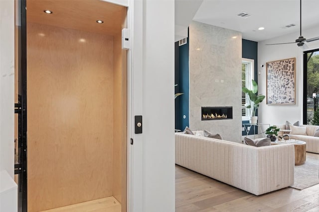 living room featuring a tile fireplace, light wood-type flooring, elevator, and ceiling fan