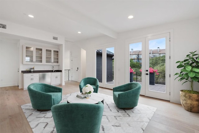 living room featuring beamed ceiling, french doors, light hardwood / wood-style floors, and indoor wet bar