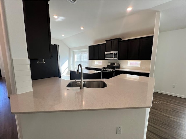 kitchen with light stone countertops, appliances with stainless steel finishes, vaulted ceiling, dark wood-type flooring, and sink