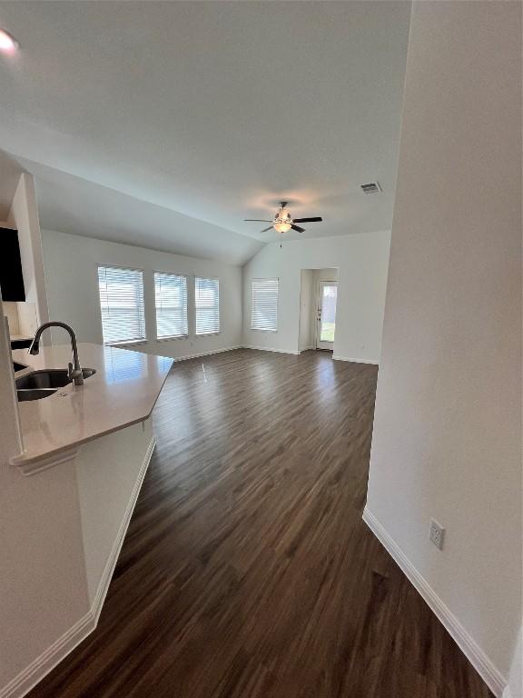 unfurnished living room featuring ceiling fan, sink, dark wood-type flooring, and vaulted ceiling