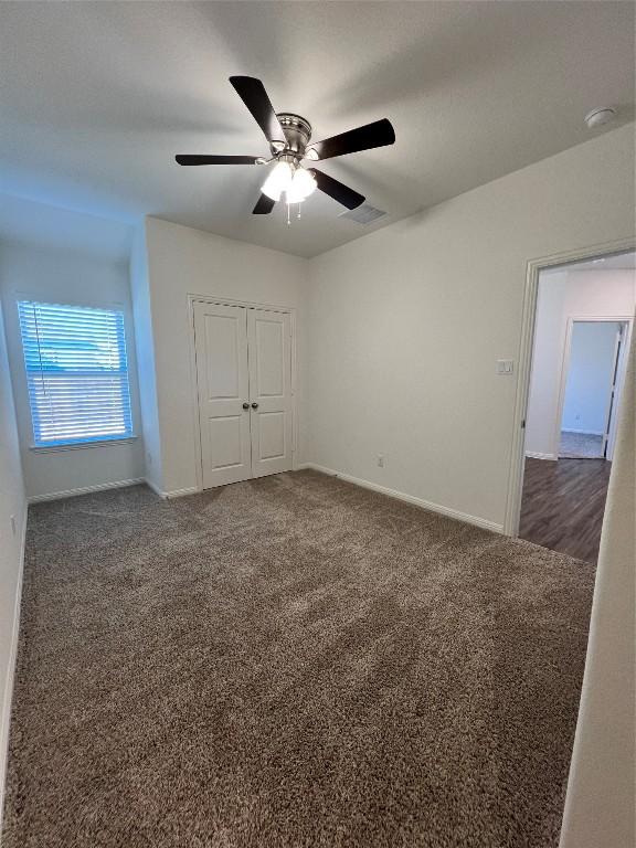 unfurnished bedroom featuring dark colored carpet, a closet, and ceiling fan