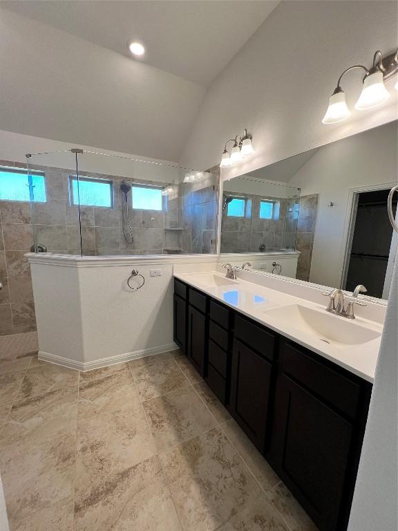 bathroom featuring a tile shower, plenty of natural light, vanity, and vaulted ceiling