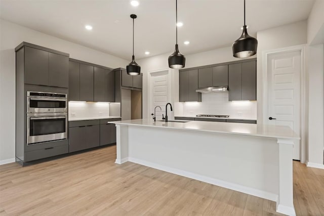 kitchen with hanging light fixtures, appliances with stainless steel finishes, and light hardwood / wood-style flooring